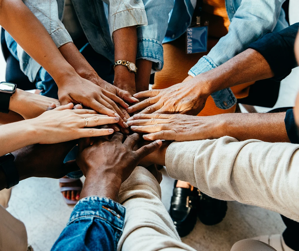 Close up on a group of people putting their hands in the centre, denoting teamwork