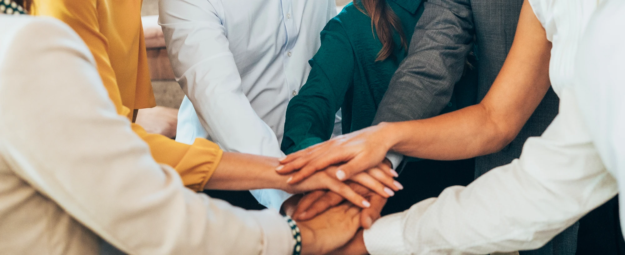 Close up on a group of people putting their hands in the centre, denoting teamwork